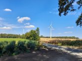Two wind turbines in a field with a blue sky