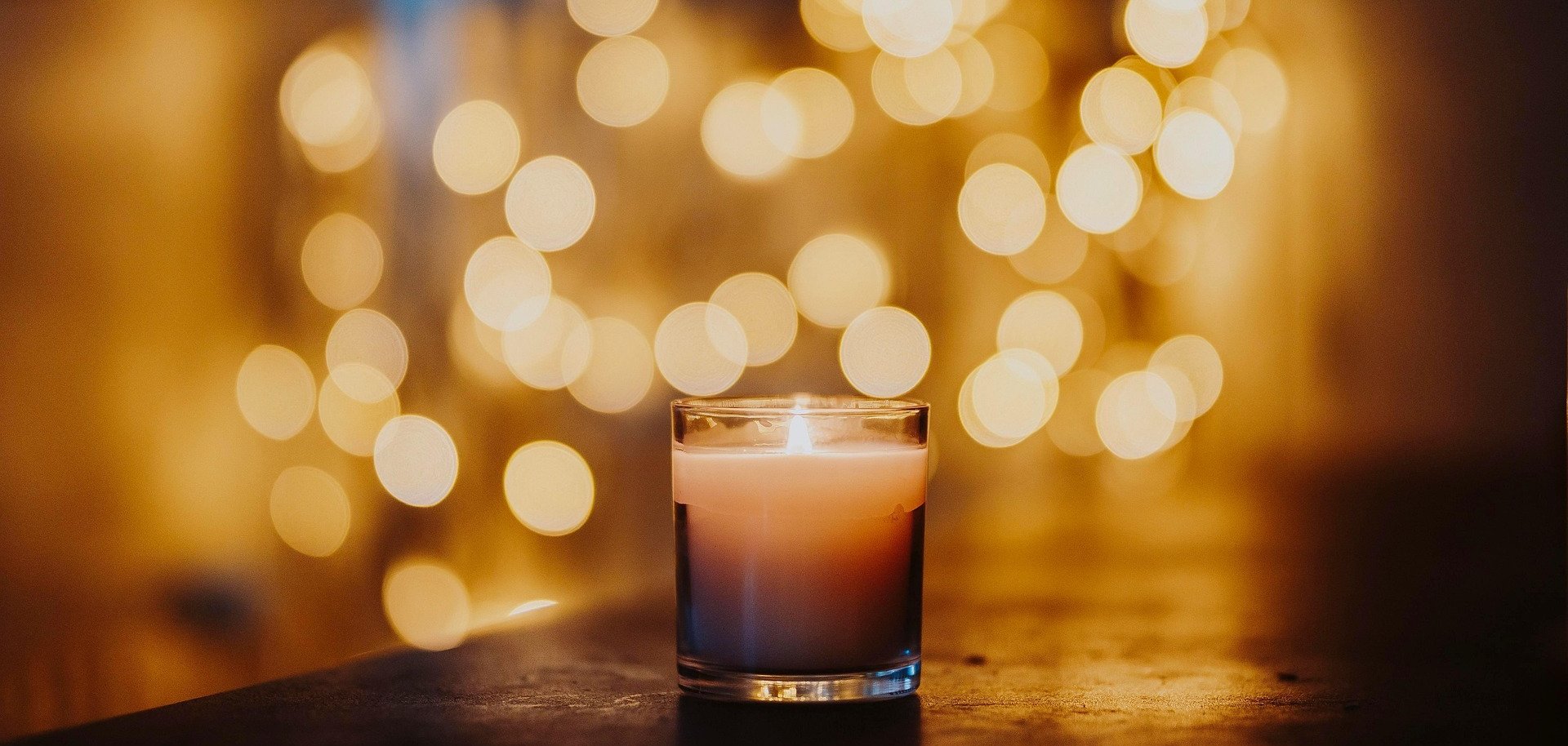 Burning candle in front of a blurred, warm light background as a Christmas symbol