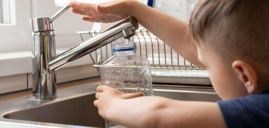 A boy fills a water bottle at the tap.