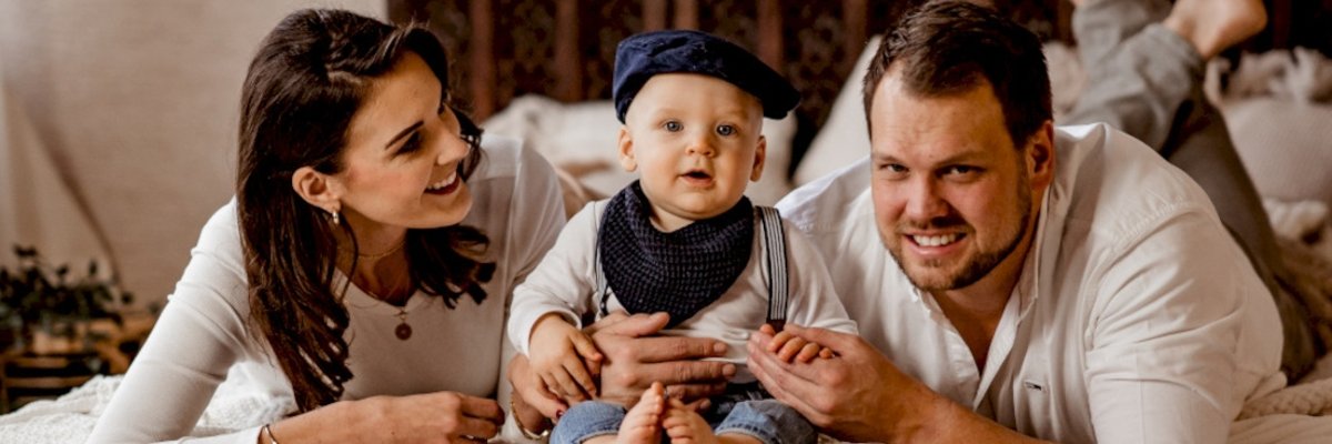 Two happy married couples (wife and husband) lying on their stomachs, with their baby laughing between them