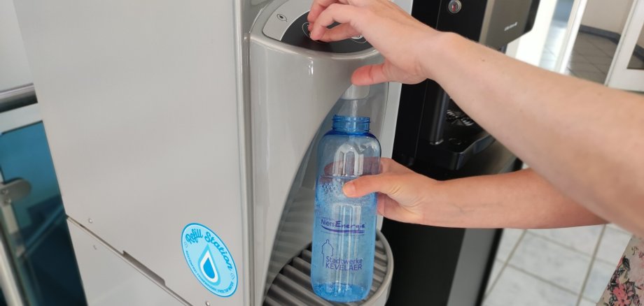 Een blauwe drinkfles wordt gevuld bij een waterdispenser.