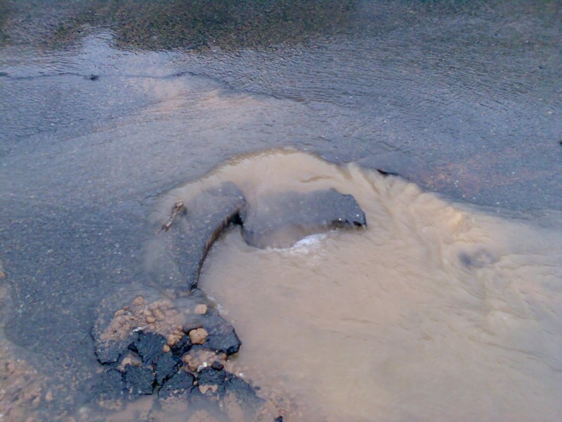 Дірка в асфальтовому покритті, з якої витікає вода
